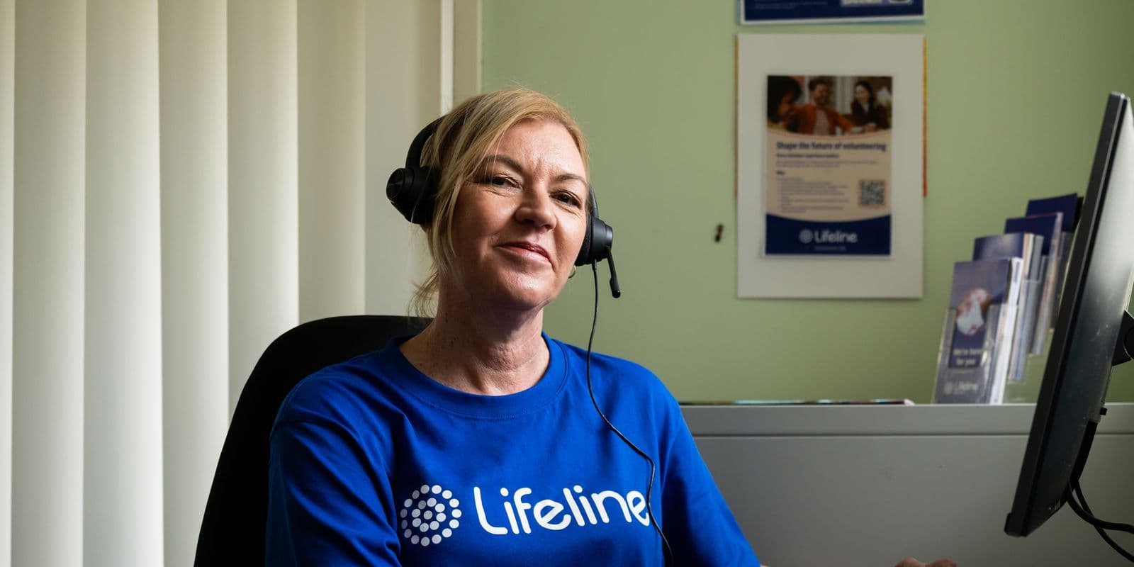 A smiling Lifeline Mid Coast Crisis Supporter on a headset at her desk